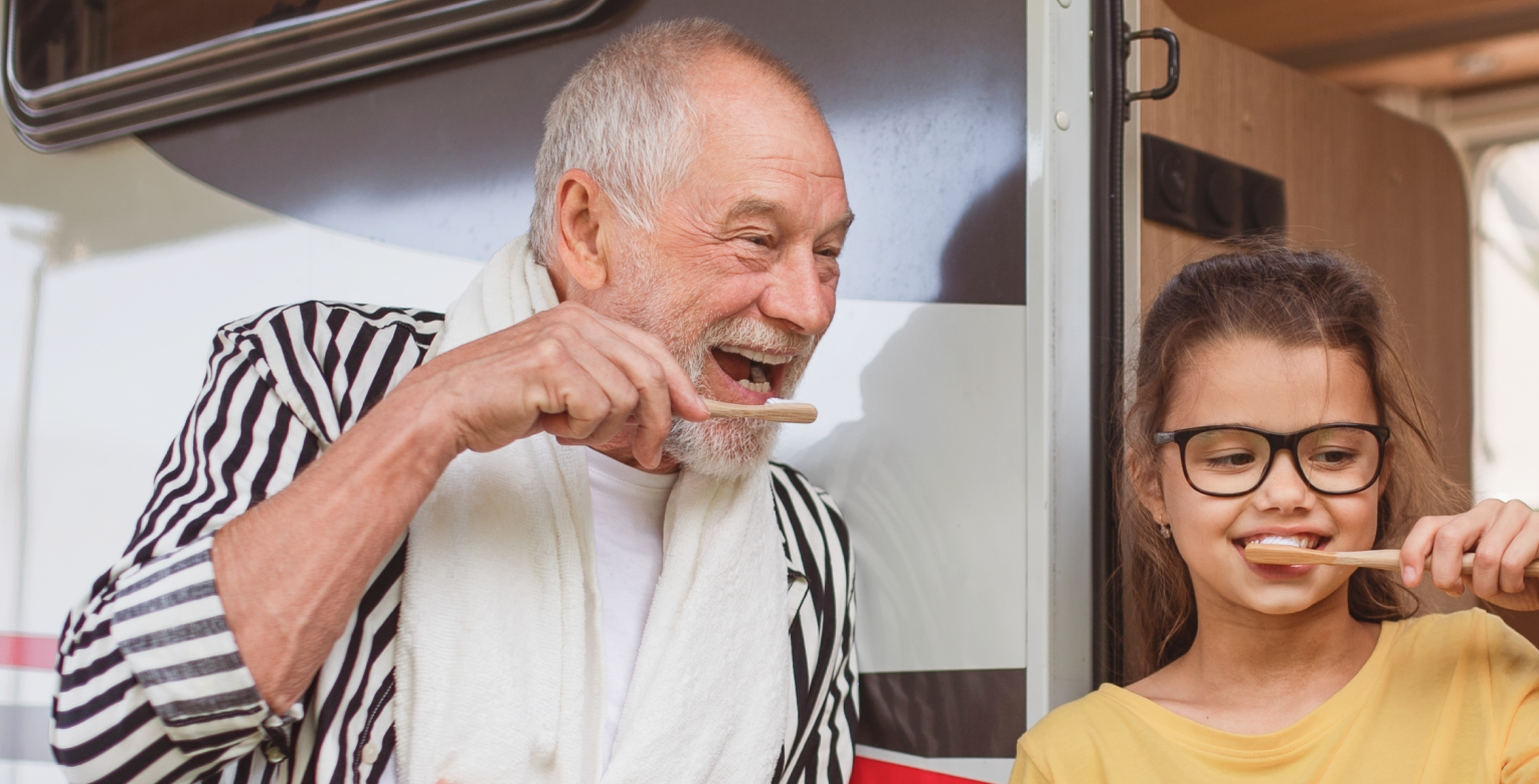 Ein älterer Mann und ein junges Mädchen putzen sich die Zähne vor einem Wohnmobil.
